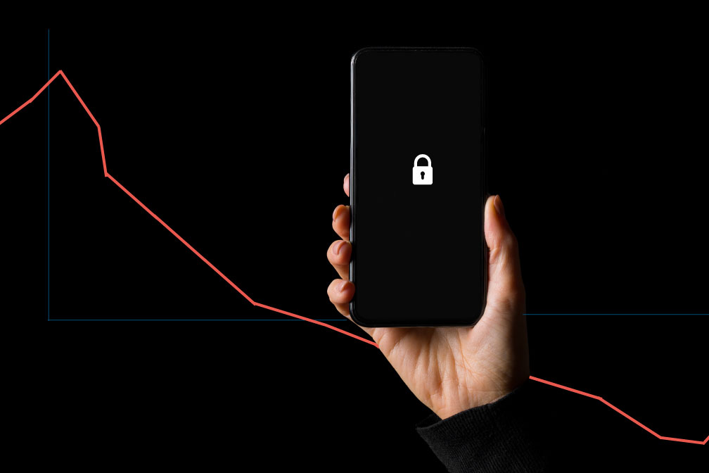 Hand holding an iphone with a lock icon on its screen in front of a graph with a downward trajectory